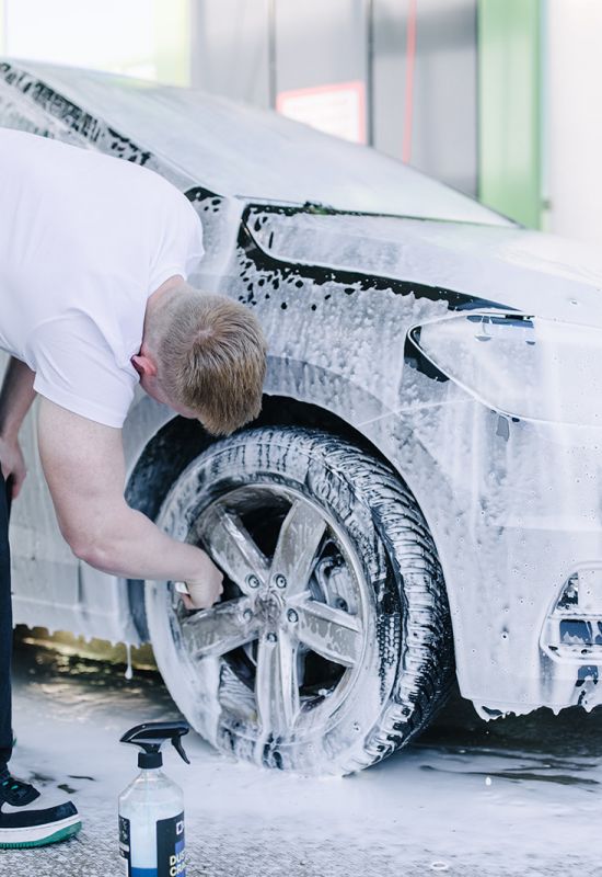 Mann reinigt Autoreifen w&auml;hrend Schaumpflege bei professioneller Au&szlig;enreinigung eines VW-Fahrzeugs