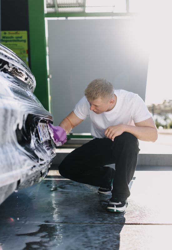 Mitarbeiter reinigt Autokennzeichen gr&uuml;ndlich mit Handschuh bei professioneller Fahrzeugw&auml;sche