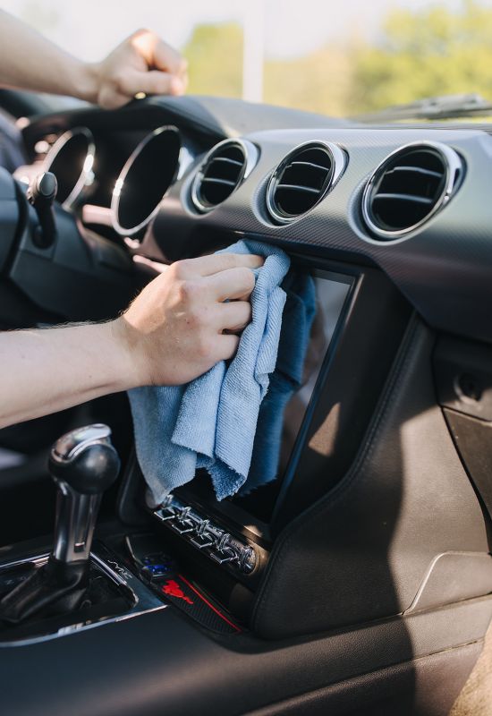 Reinigung des Touchscreens und Armaturenbretts im Auto mit Mikrofasertuch bei der professionellen Innenaufbereitung