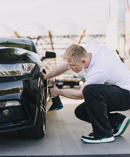 Autopfleger behandelt Reifen eines schwarzen Ford Mustang mit Pflegeprodukt bei professioneller Fahrzeugaufbereitung