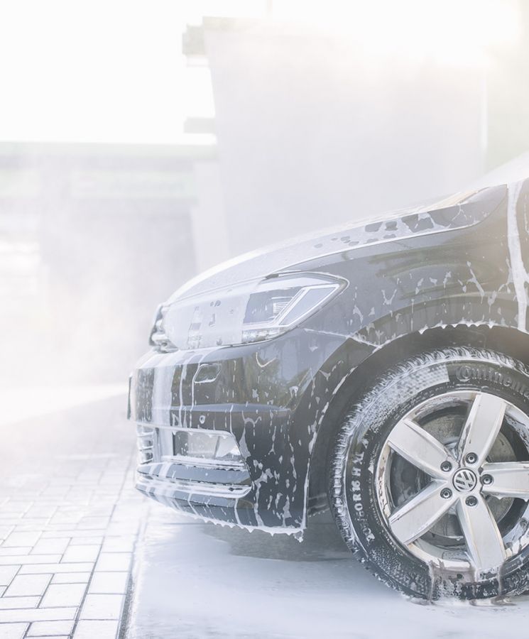 Vorderansicht eines eingesch&auml;umten VW bei der Au&szlig;enw&auml;sche &ndash; Fahrzeugpflege mit Schaumreiniger im Sonnenlicht